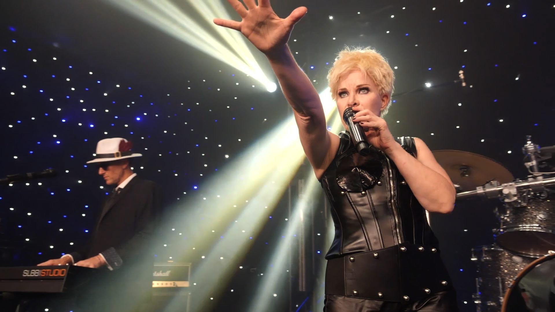 Kelly Corsino reaching into beams of stage light while singing
